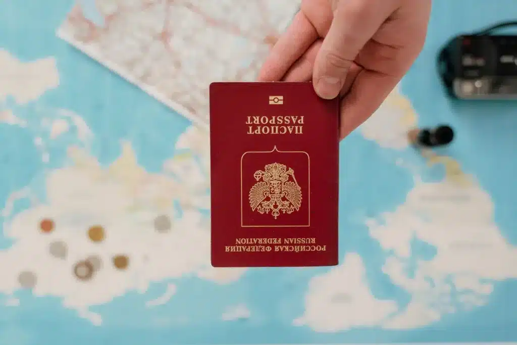 Manos sosteniendo un pasaporte abierto y documentos de visa en un escritorio de consulado